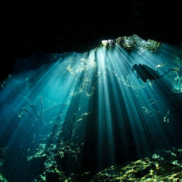 یک غواص اسکوبا در حال شنا زیر تابش نور خورشید در غار زیرزمینی مکزیک